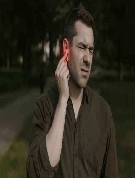 Man holding his ear, possibly experiencing pain or discomfort, outdoors.