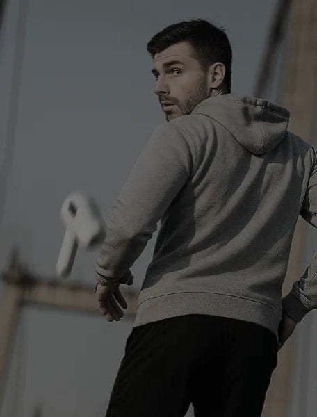 Man in a gray hoodie and black pants standing outdoors with a blurred background lost earphones