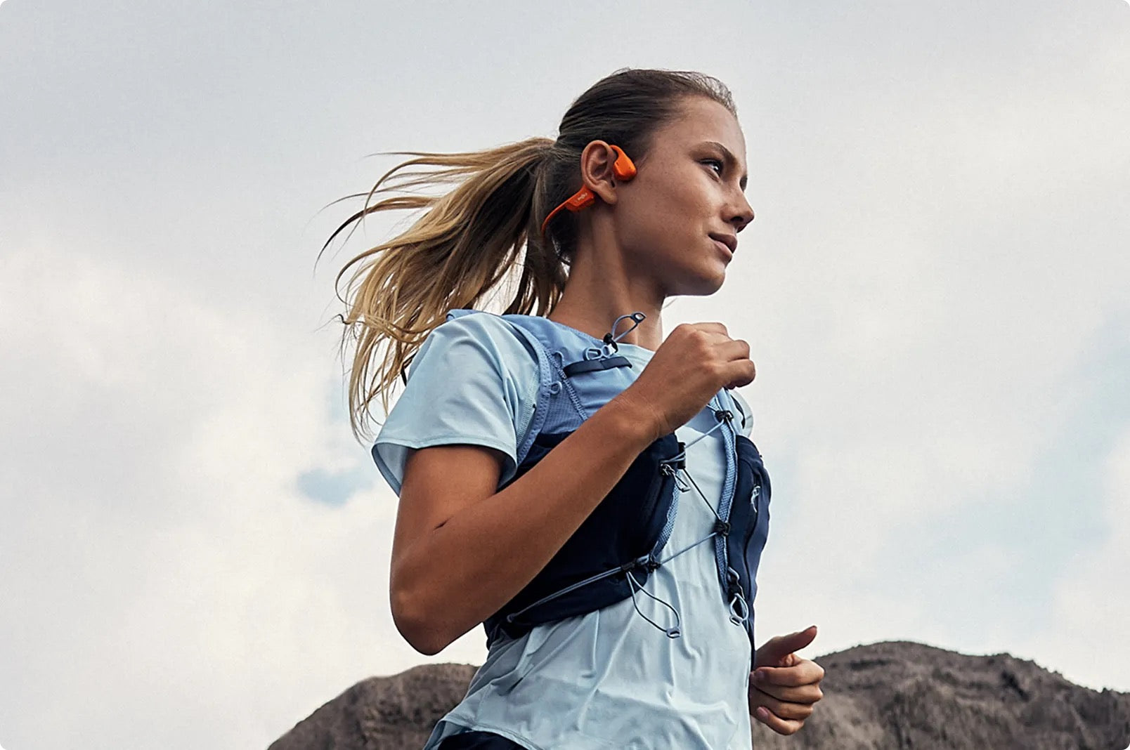 Open Ear Headphones best workout headphones. Woman running outdoors with mountains in the background