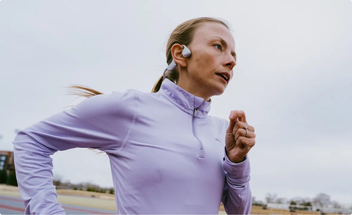 -Dakota Popehn - 2021 and 2022 Grandmas Marathon Champion, Bone Headphones, open-ear technology, running outdoors wearing a light purple jacket with earbuds.